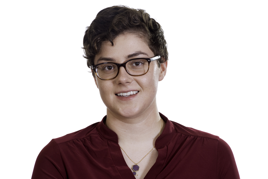 This Brian Charles Steel photo is a headshot of a white woman with short curly brown hair.  She is wearing a red blouse, glasses, and a necklace.  She is centered in the frame, and the background is completely white.  She is lit in a Rembrandt style. 